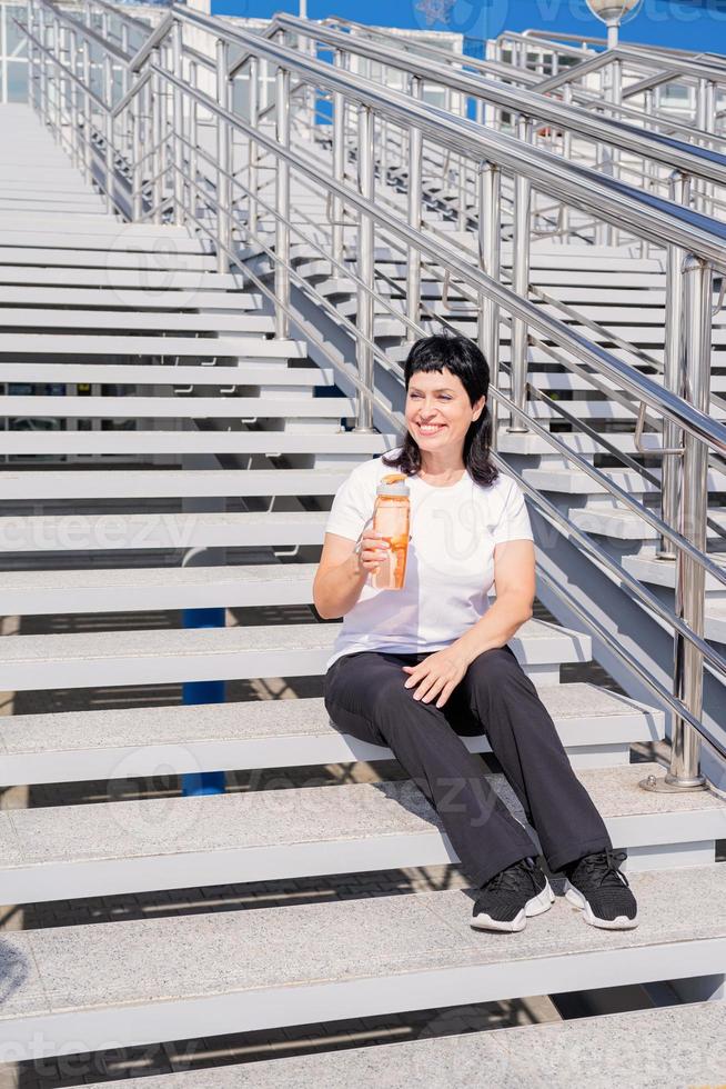 femme âgée buvant de l'eau après l'entraînement à l'extérieur sur fond urbain photo