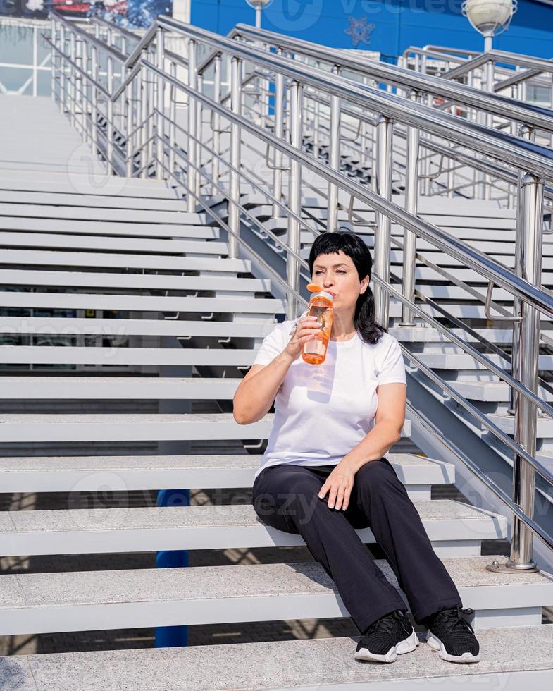 femme âgée buvant de l'eau après l'entraînement à l'extérieur sur fond urbain photo