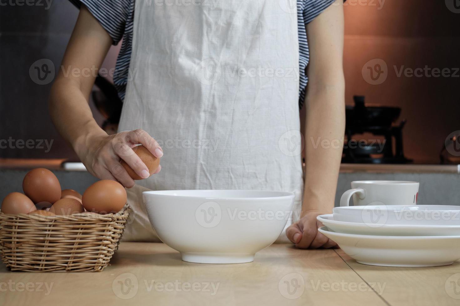 une cuisinière dans un tablier blanc casse un œuf dans la cuisine de la maison. photo