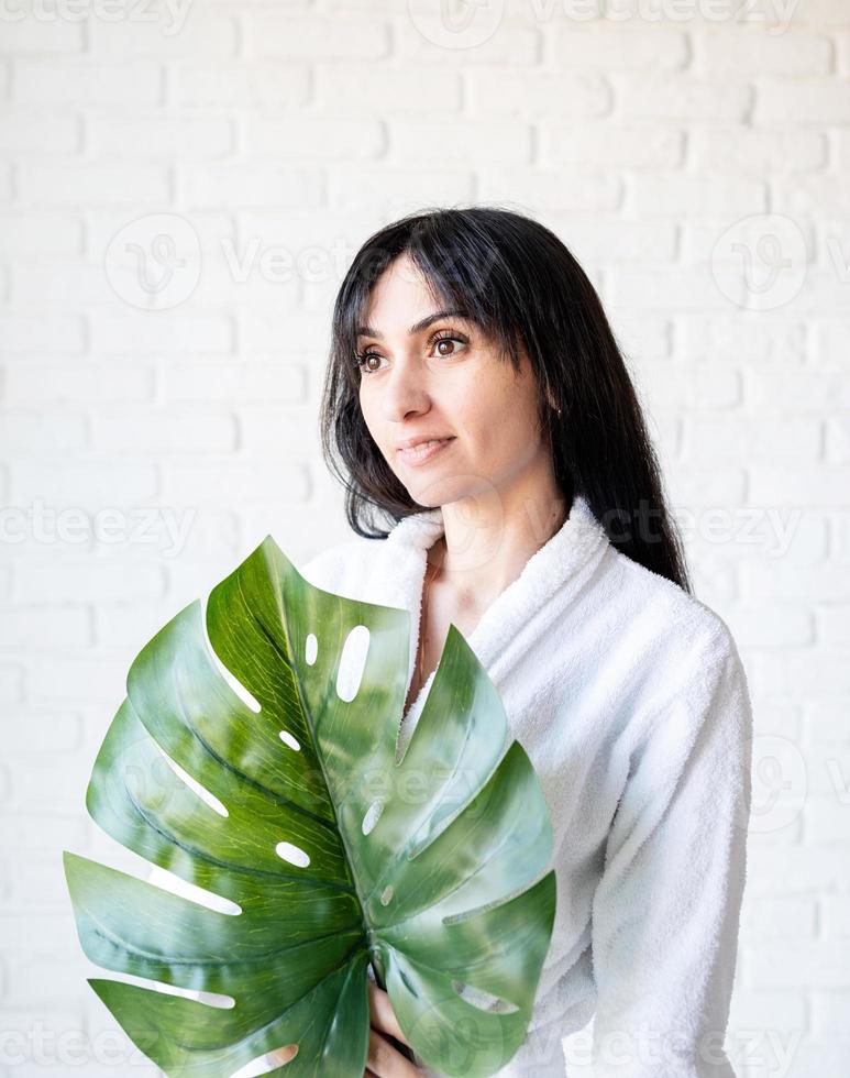 Femme du Moyen-Orient portant des serviettes de bain tenant une feuille de monstera verte photo