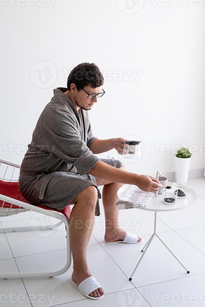 homme assis en peignoir faisant du thé à la maison photo