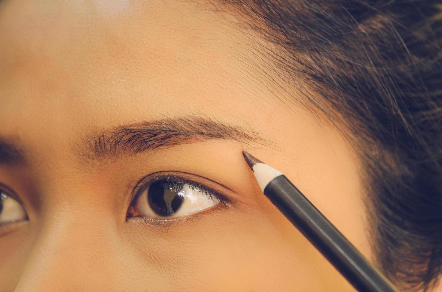 visage de beauté d'une femme asiatique en appliquant un crayon à sourcils sur la peau. photo