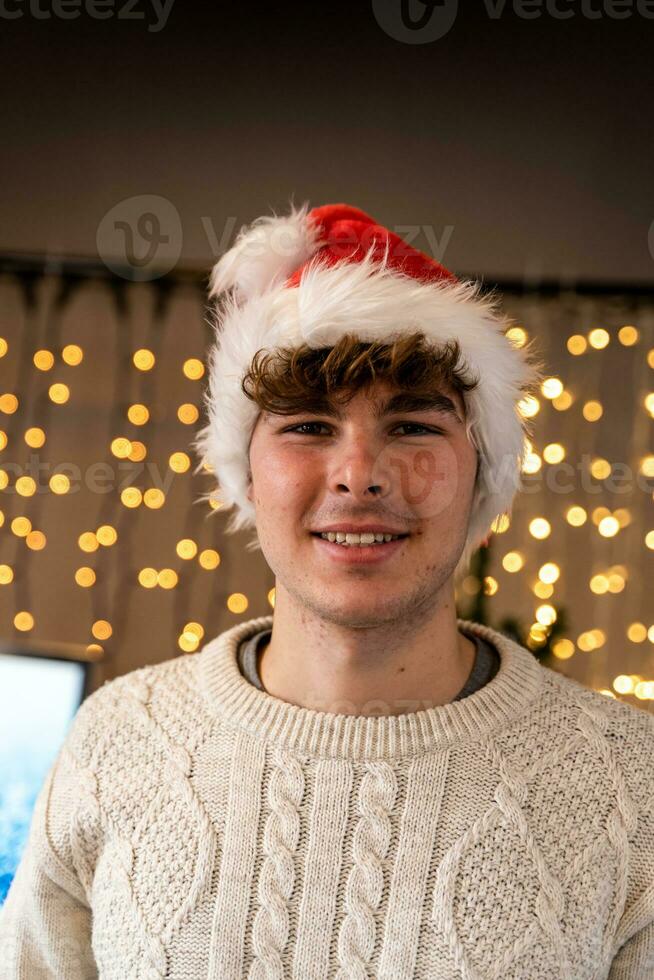 portrait de souriant Jeune homme portant rouge chapeau dans de face de une mur de Noël lumières photo