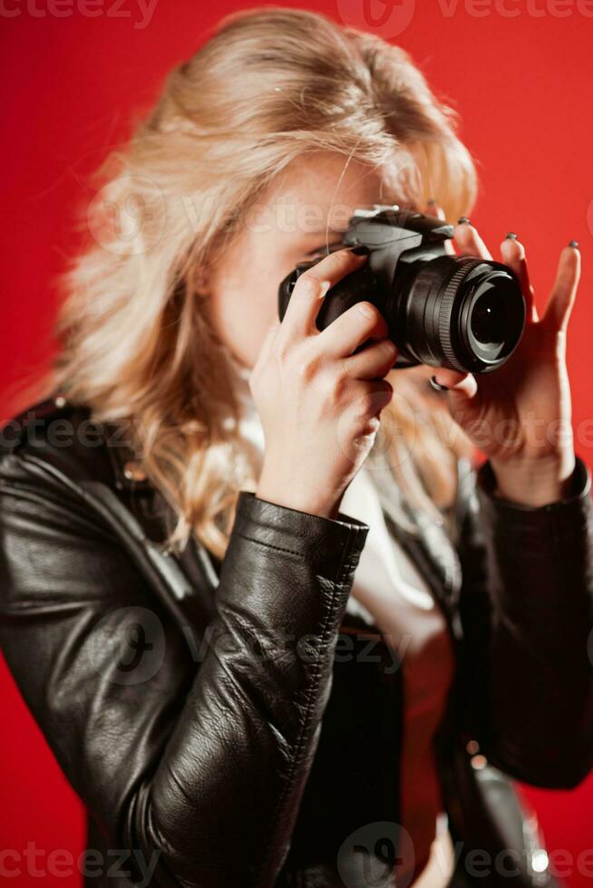 portrait de une magnifique fille photographe avec une caméra dans sa mains qui est photographié dans une photo studio sur une rouge Contexte