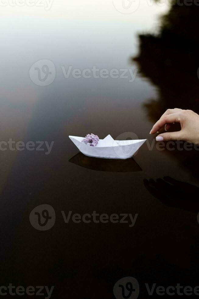 papier bateau fabriqué de papier, le bateau va sur le eau, une brin de lilas sur le bateau, je lancement le bateau dans le l'eau photo