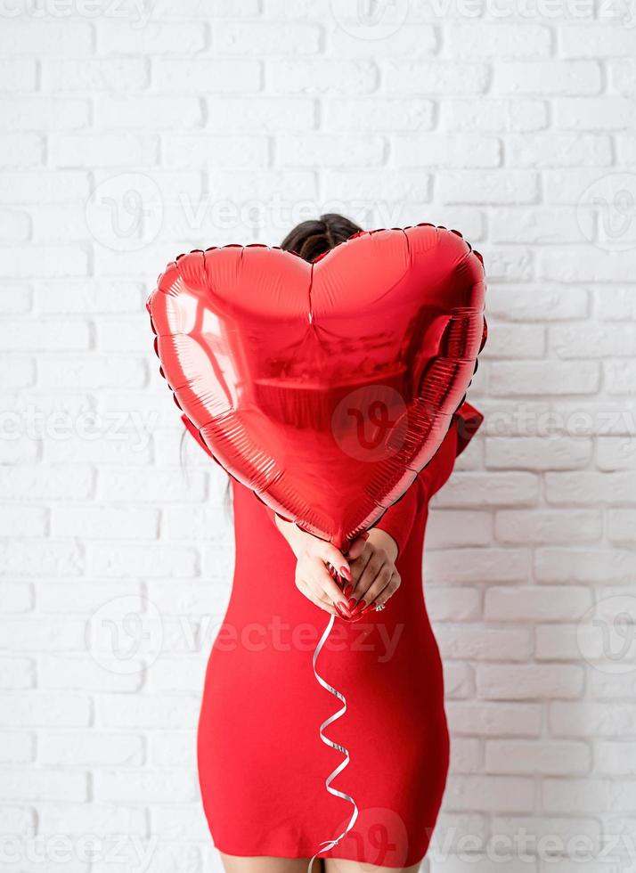 Jeune femme brune en robe rouge tenant un ballon coeur rouge photo