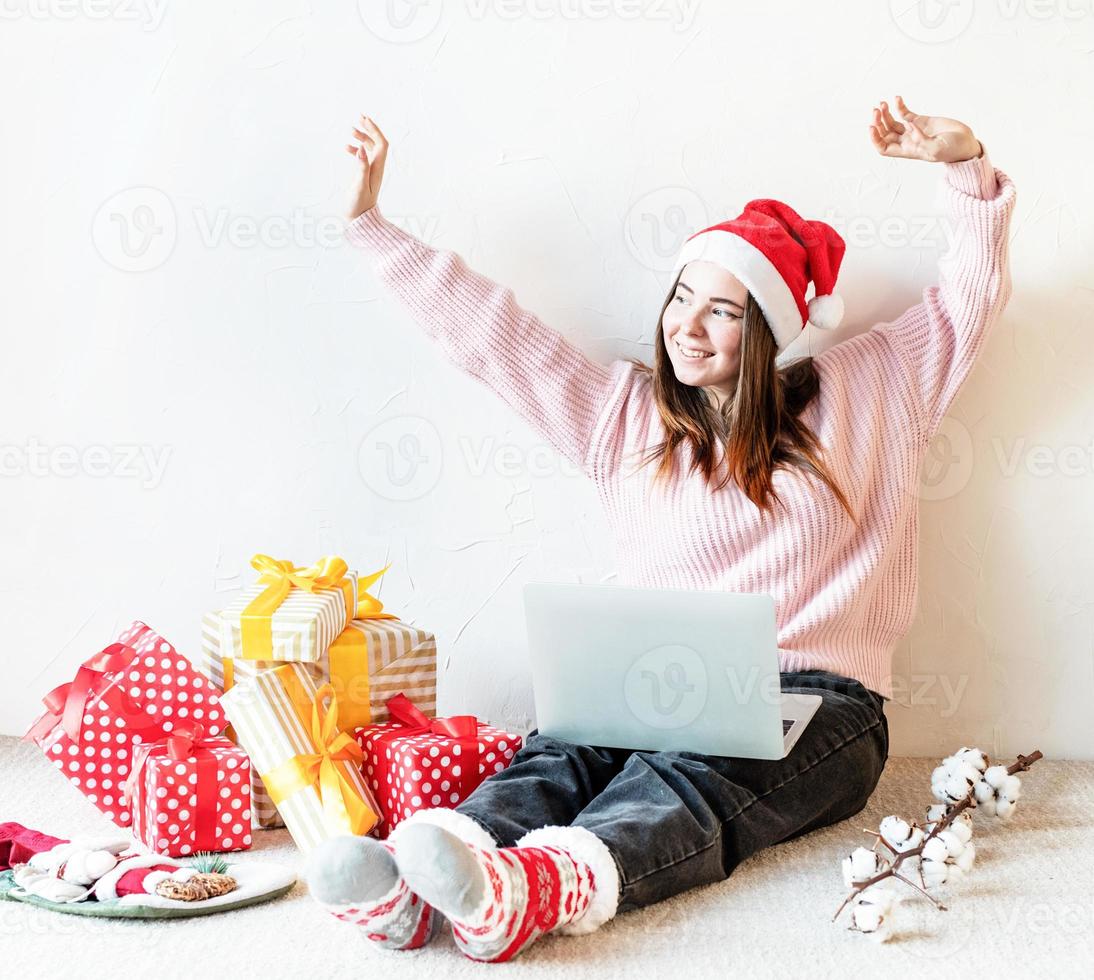 Jeune femme à santa hat shopping en ligne entourée de cadeaux photo