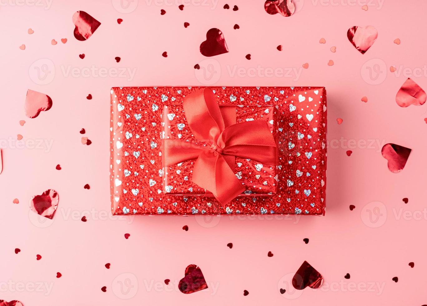 coffret cadeau rouge avec noeud de corde sur fond rose avec des confettis coeur photo