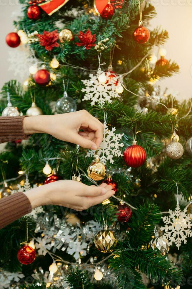 femelle main décorer Noël arbre avec jouets. lumière du soleil inondations le vivre chambre. photo