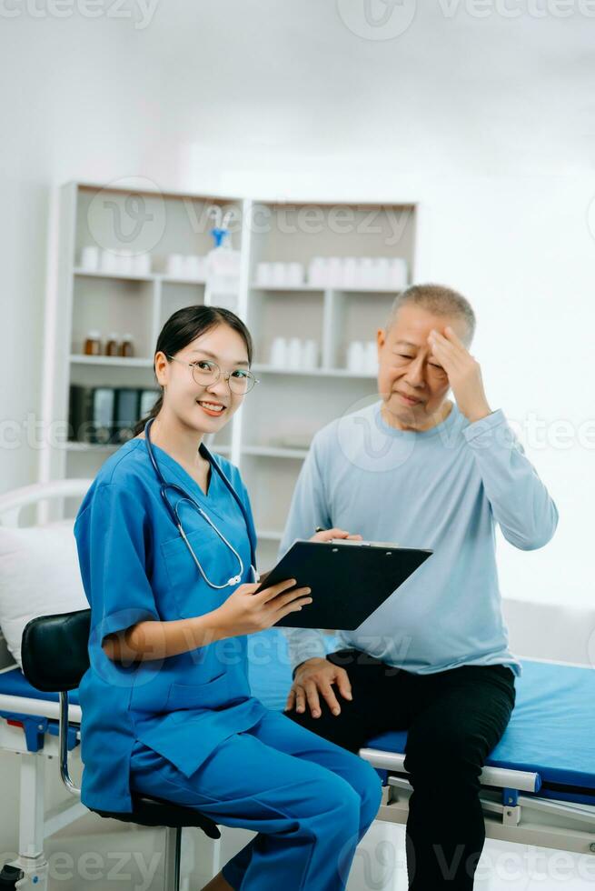 asiatique médecin dans blanc costume prendre Remarques tandis que discuter et asiatique âgé, homme patient qui mensonge sur lit avec recevoir saline Solution dans hôpital ou clinique. photo