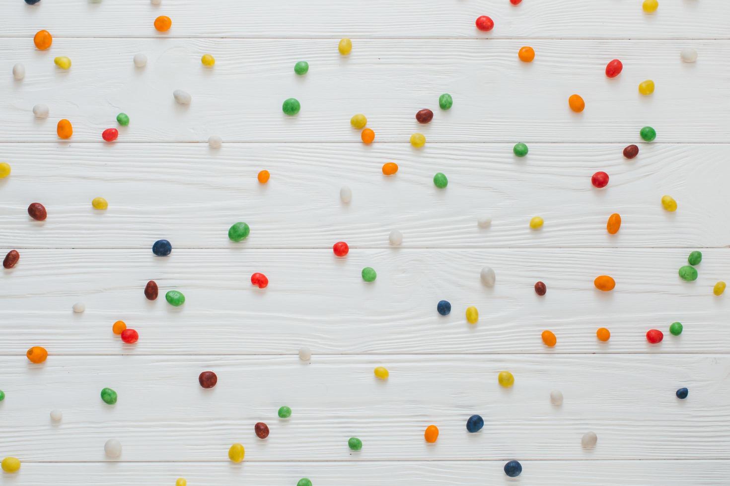 de nombreux bonbons sucrés multicolores sur fond de bois blanc. photo