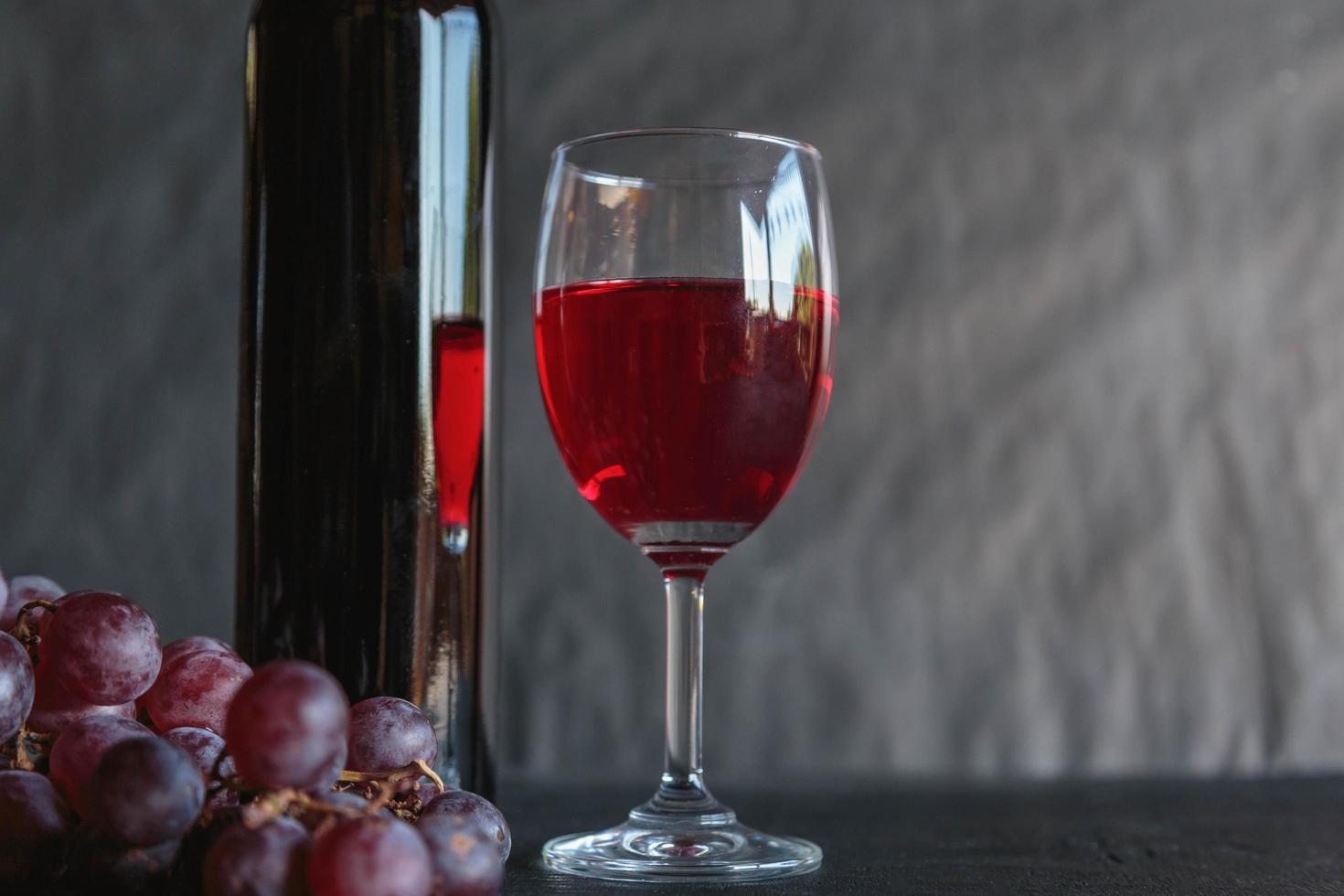 vin rouge et bouteille de vin avec des raisins sur fond noir photo