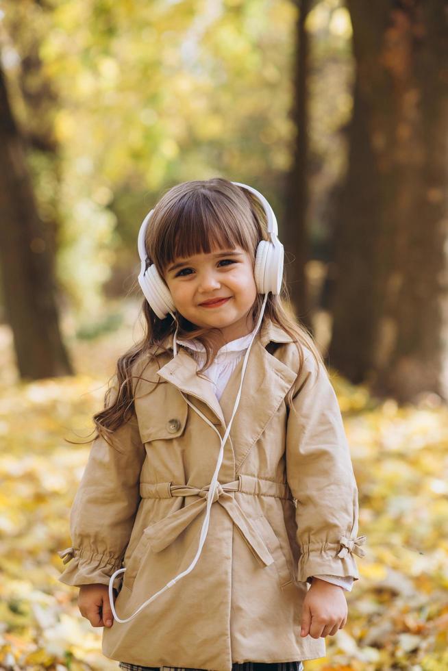 heureuse petite fille écoutant de la musique au casque dans le parc en automne. photo