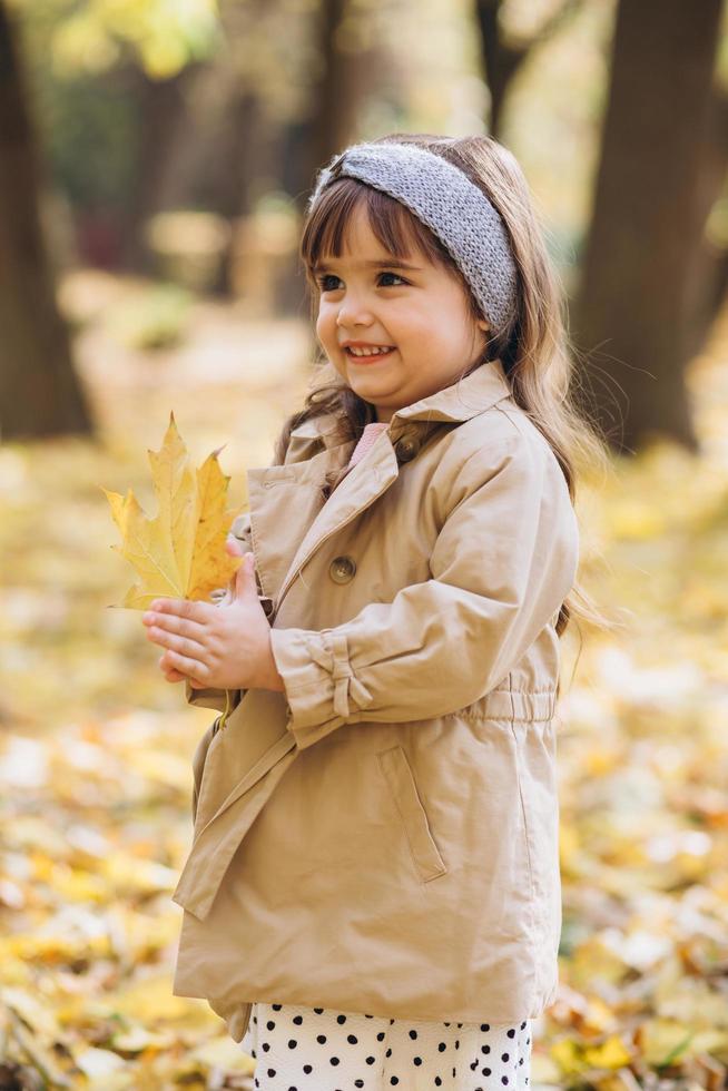 heureuse petite fille tenant une feuille d'érable jaune dans le parc en automne photo