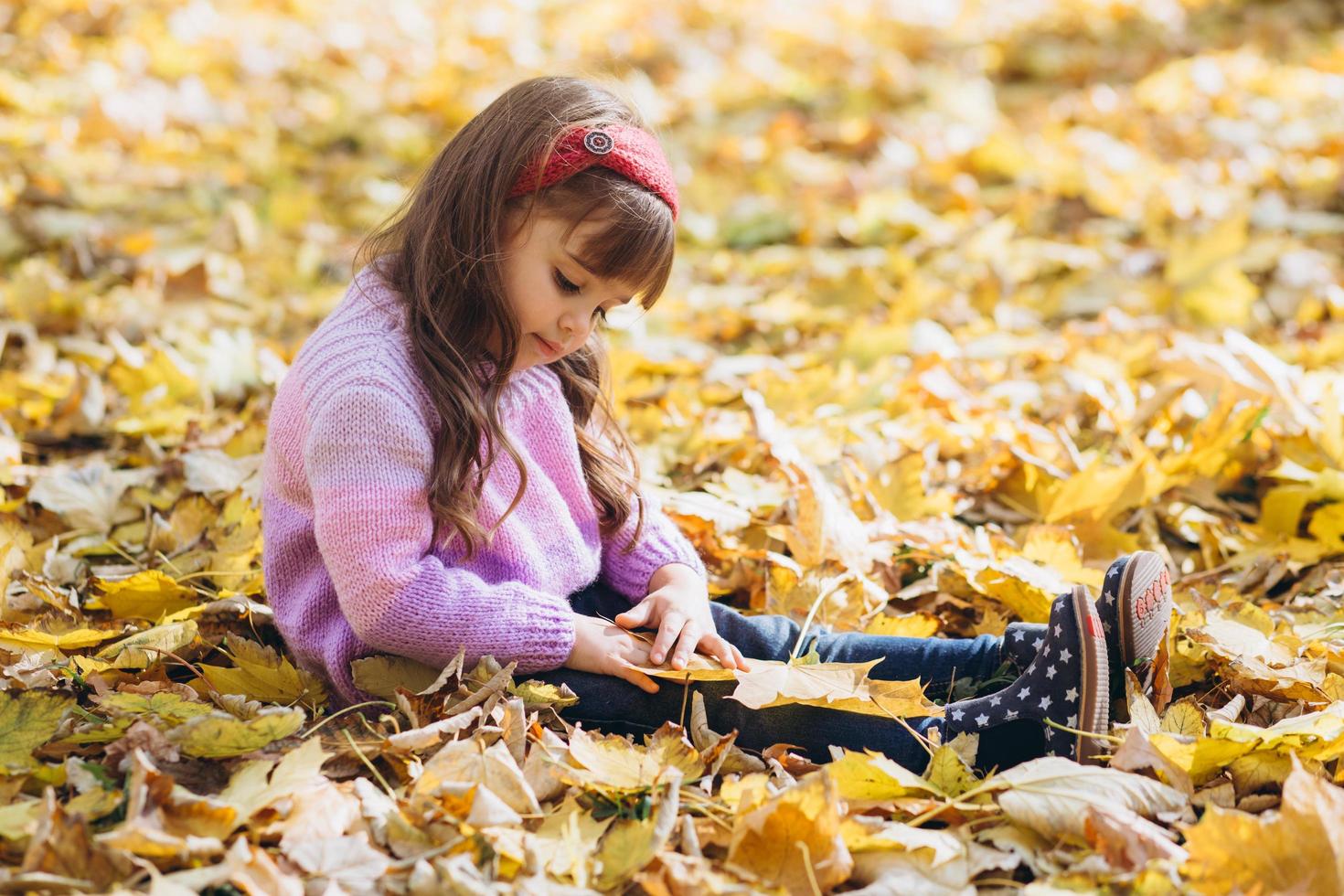 heureuse petite fille assise parmi les feuilles d'automne jaunes dans le parc photo