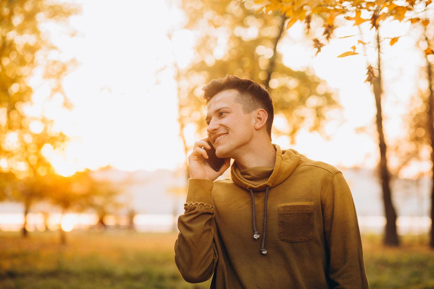 mec heureux souriant et parlant au téléphone dans le parc en automne photo