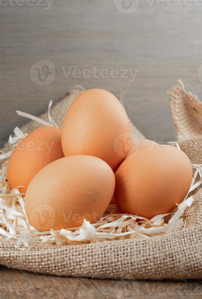 oeufs biologiques frais en toile de jute avec de l'herbe sèche sur une table en bois photo