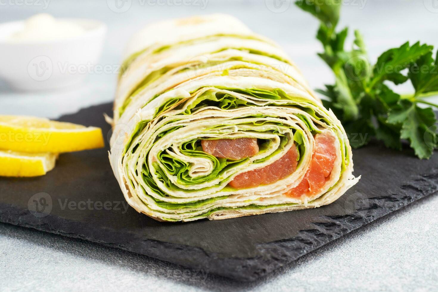 rouleaux de pain pita fin et de saumon salé rouge avec des feuilles de laitue sur un support en ardoise, fond de béton gris. espace de copie. photo