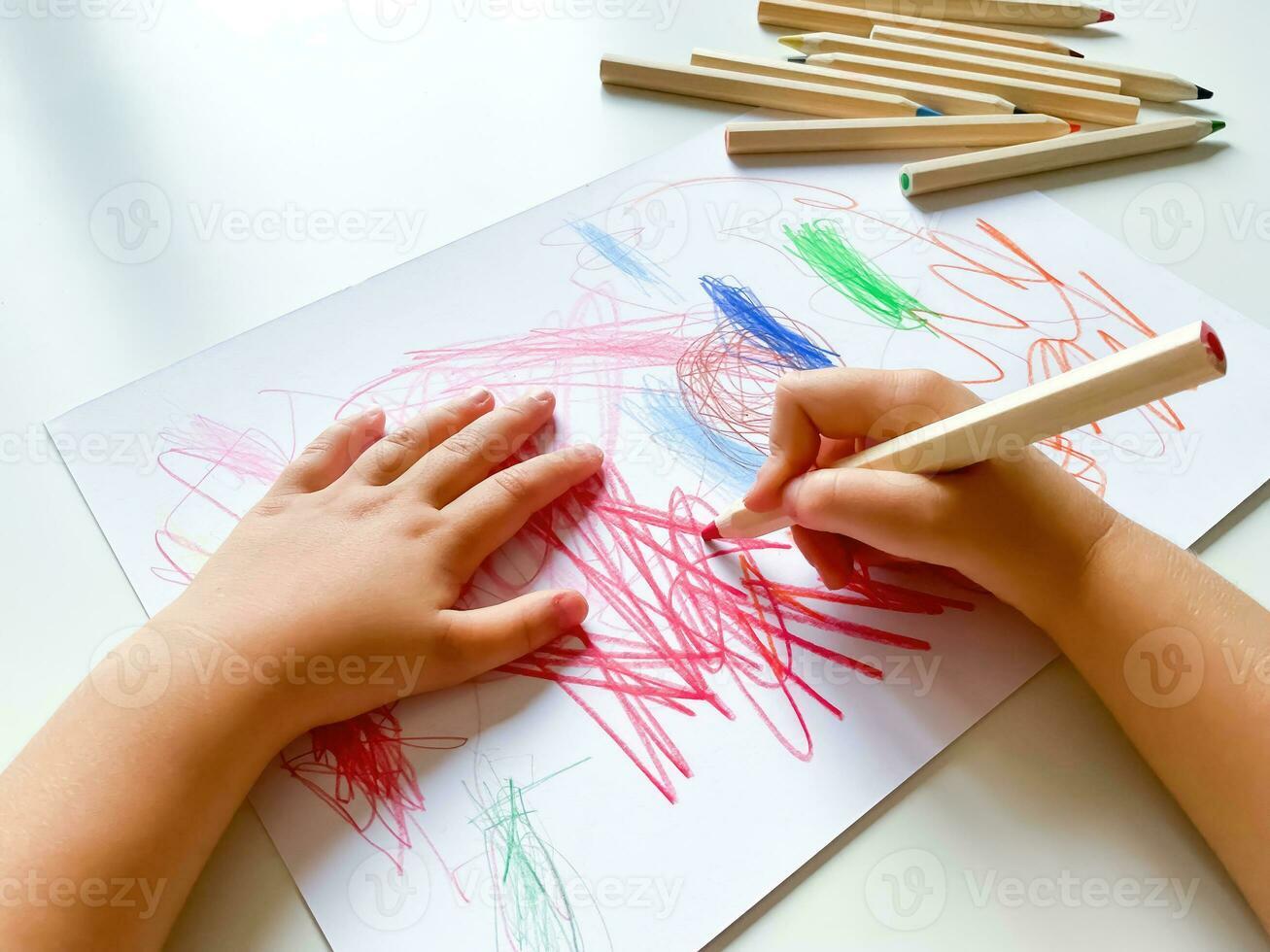 petit enfant dessine avec coloré des crayons sur papier sur blanc tableau. photo