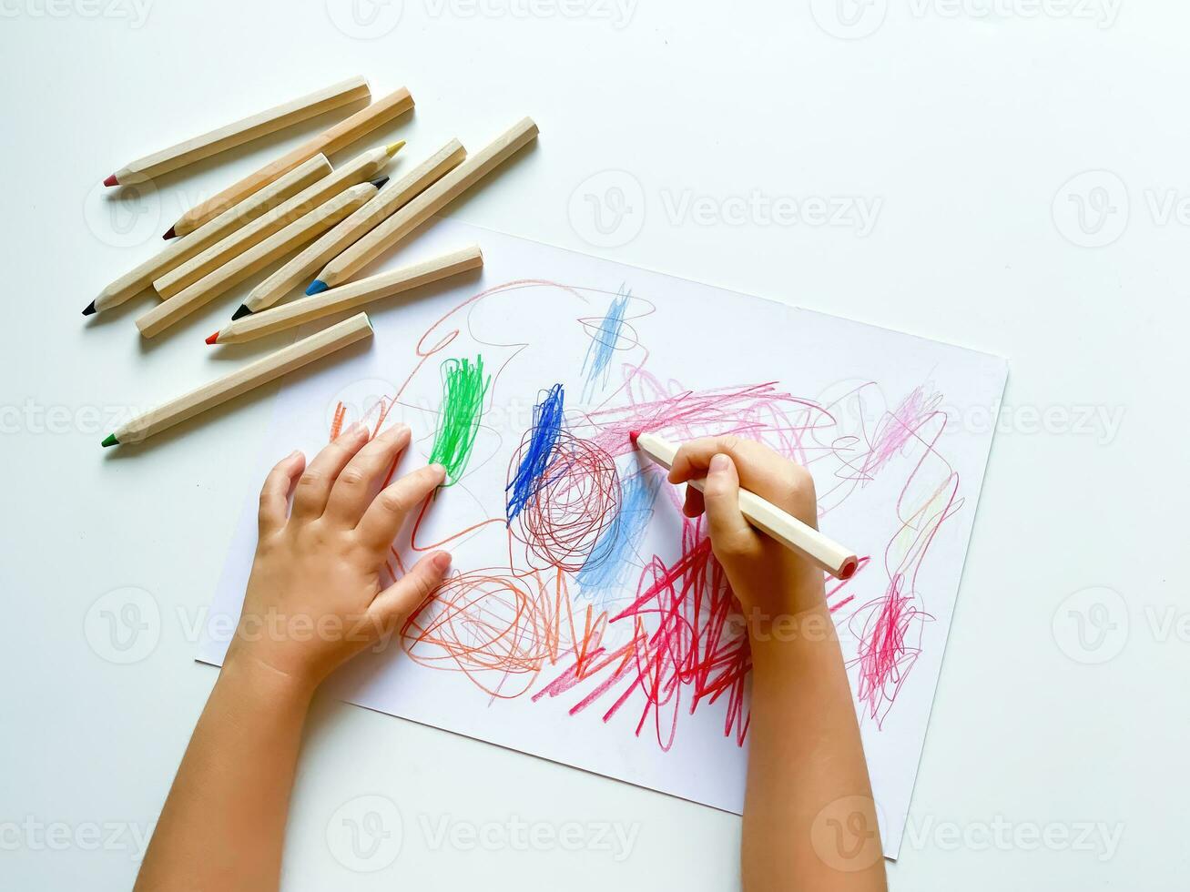 petit enfant dessine avec coloré des crayons sur papier sur blanc tableau. photo