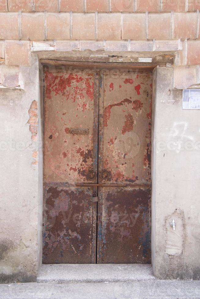 Ancien bâtiment de maison en béton endommagé et porte en bois rouge photo