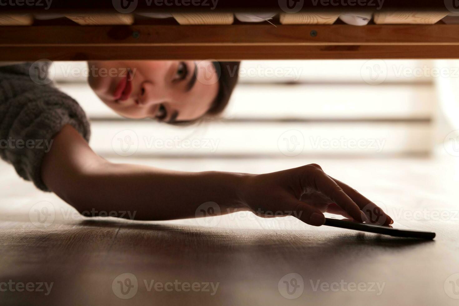 fermer coup de fille qui prend une téléphone intelligent de en dessous de le lit photo