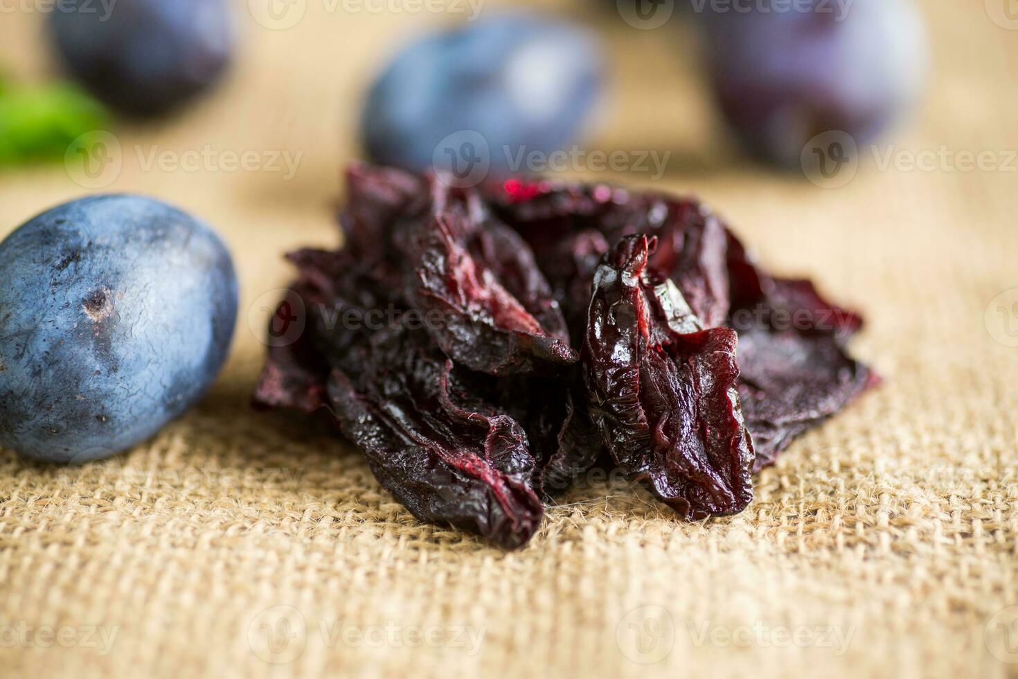 séché pruneaux dans une cuillère sur une toile de jute nappe de table contre une Contexte de Frais prunes. photo