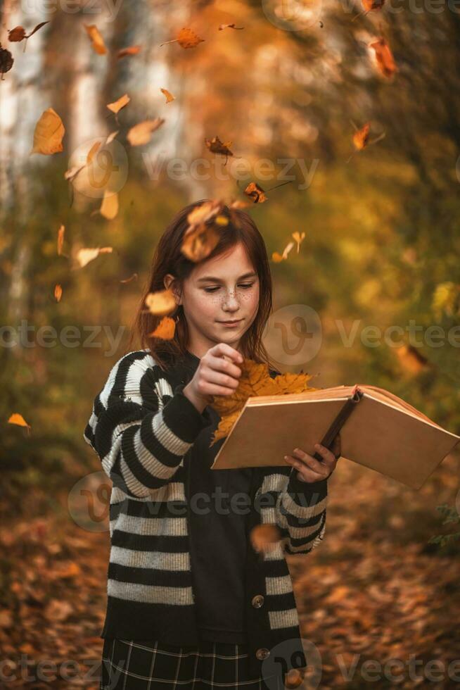 fille avec taches de rousseur avec une livre parmi l'automne feuilles photo