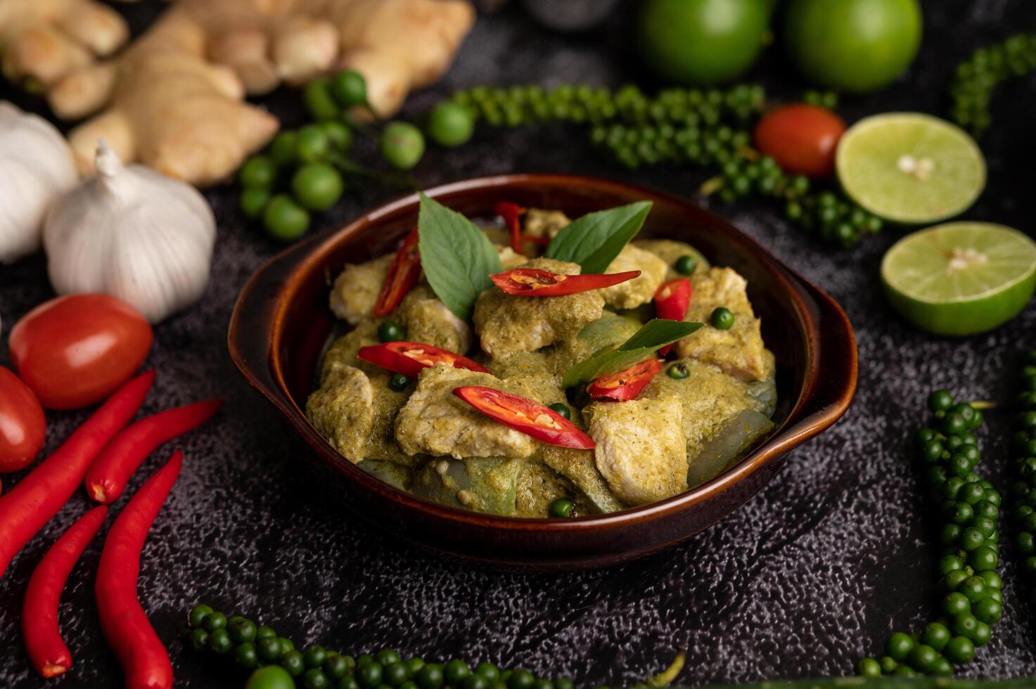 curry vert de porc dans un bol marron avec des épices sur un ciment noir photo