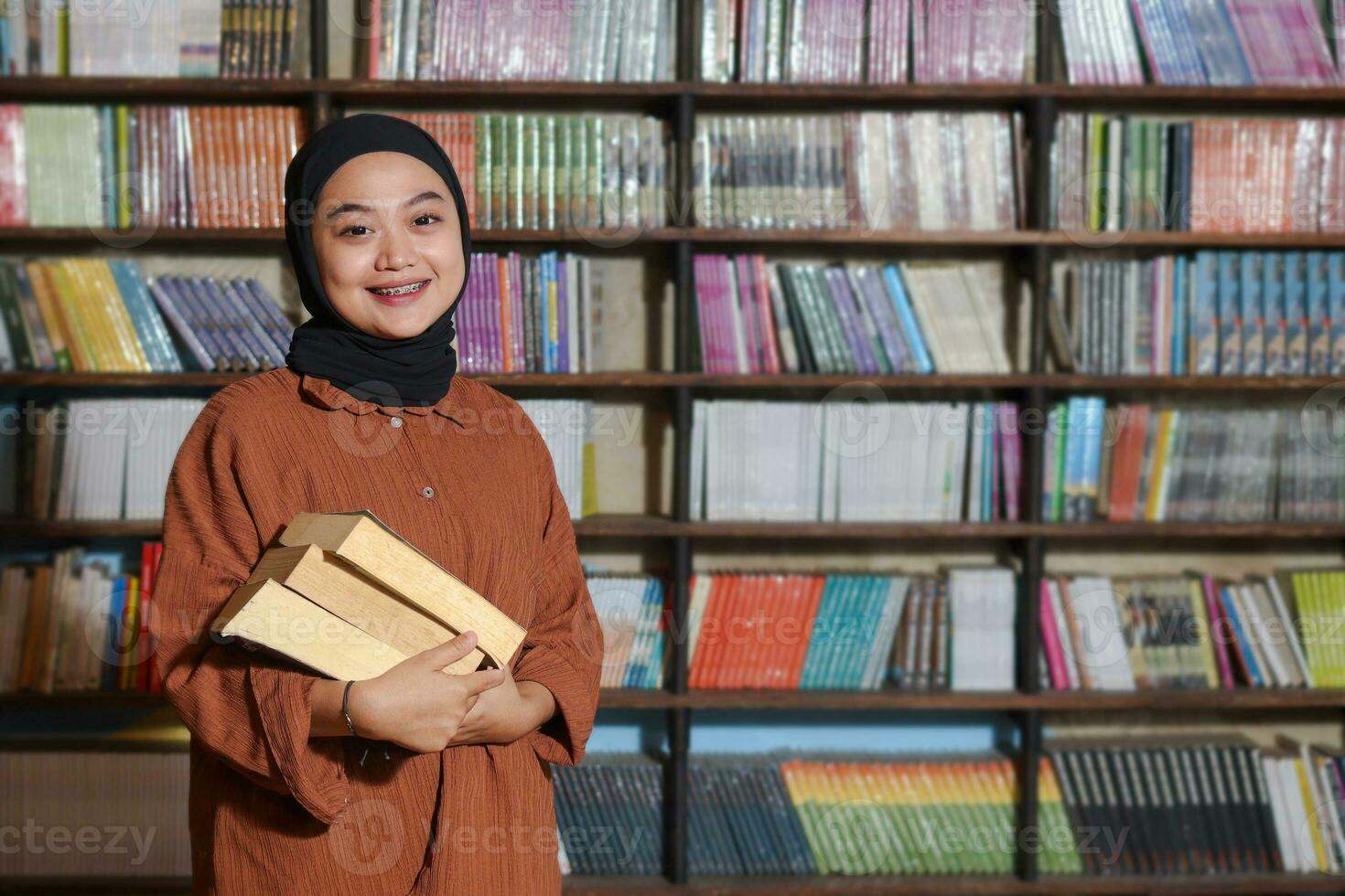 portrait de asiatique hijab femme en portant livre dans de face de bibliothèque étagère à livres. musulman fille en train de lire une livre. concept de l'alphabétisation et connaissance photo