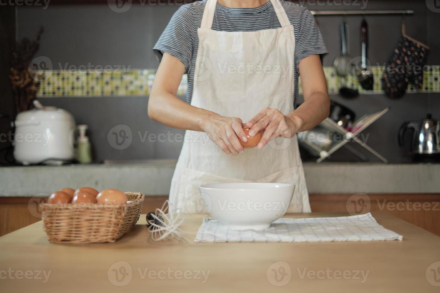 une cuisinière dans un tablier blanc casse un œuf dans la cuisine de la maison. photo