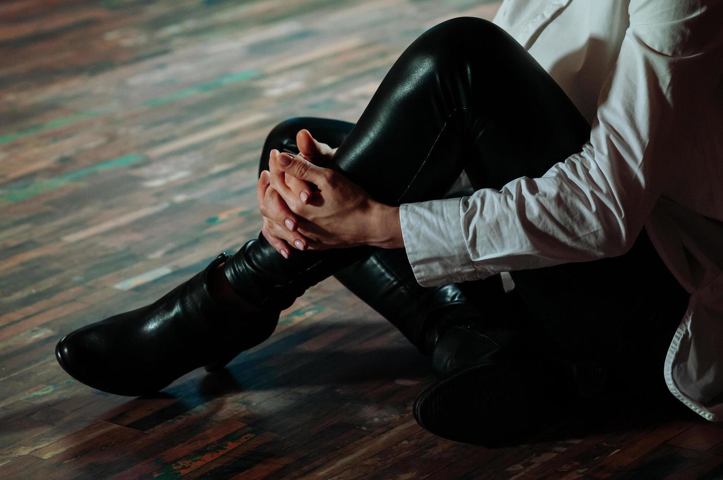 Femme en pantalon de cuir noir assis sur le sol dans une pièce sombre photo