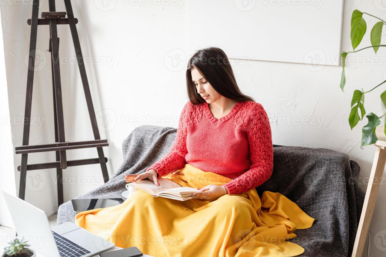 femme lisant assise sur le canapé avec plaisir dans des vêtements décontractés photo