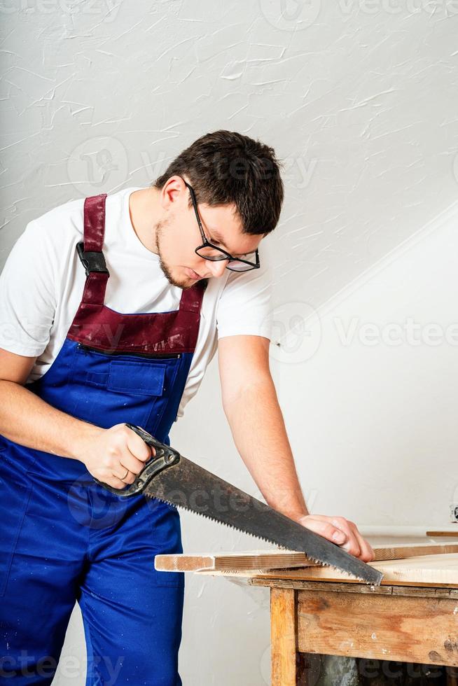 charpentier en salopette bleue sciant une planche avec une scie à main photo