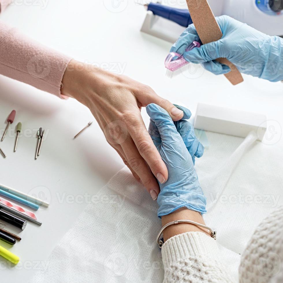 maître de manucure en gants à l'aide d'une lime à ongles pour polir l'ongle d'un client photo