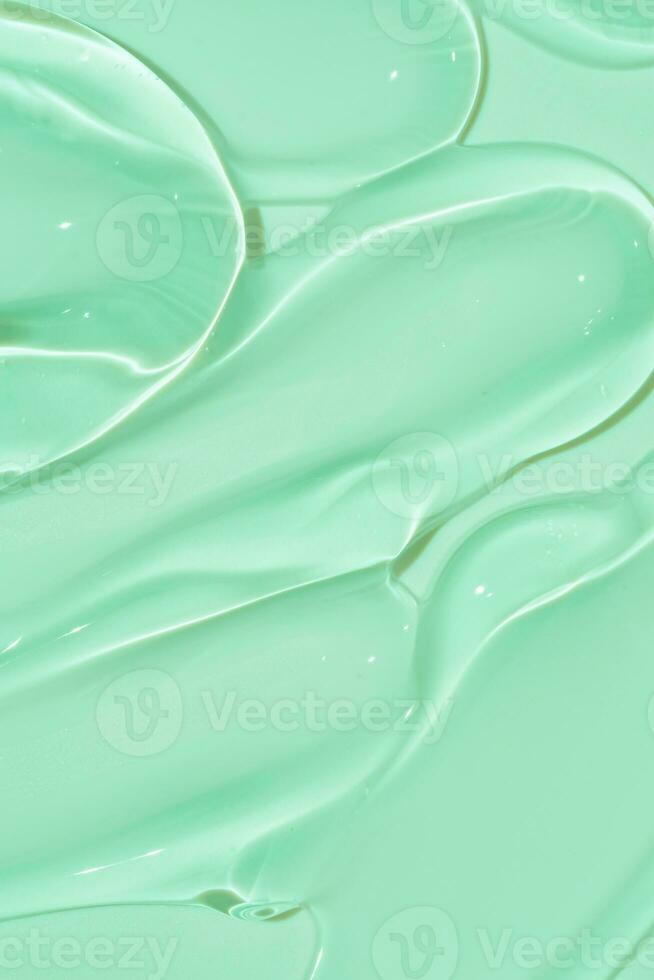 texture crème de frottis cosmétiques sur fond vert. goutte de sérum de beauté. échantillon de produit de soin de la peau transparent et crémeux. photo