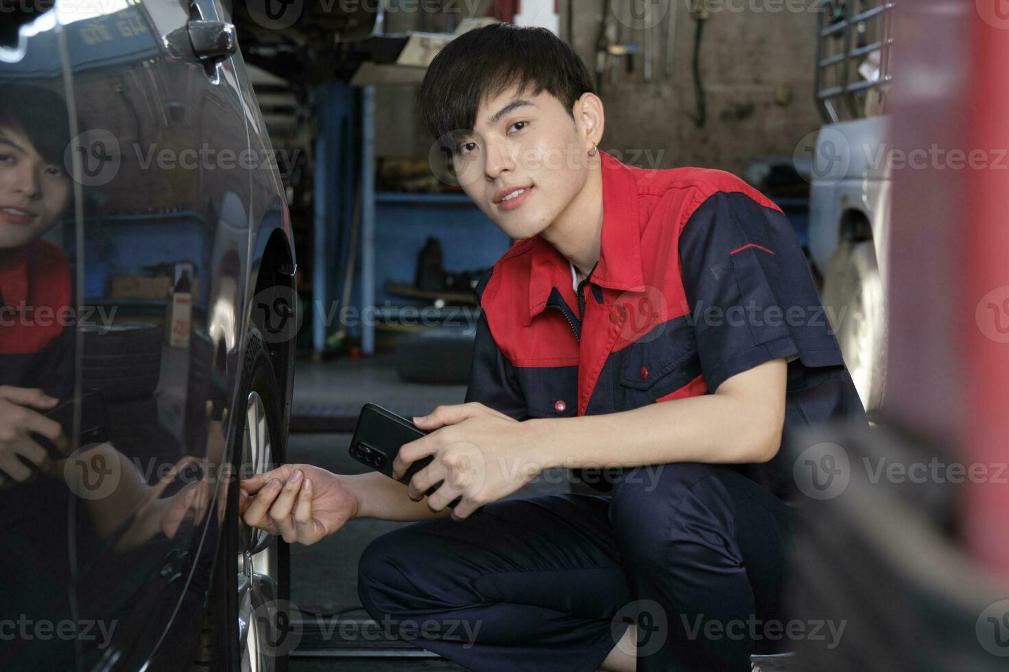 Jeune Masculin asiatique professionnel automobile mécanicien ouvrier chèques pneu pression par téléphone intelligent application à une voiture garage, expert dans entretien véhicule service, et fixation métiers auto industrie. photo