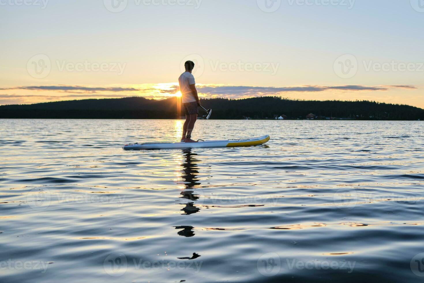 une homme sur une pagayer planche dans le des rayons de Soleil. photo