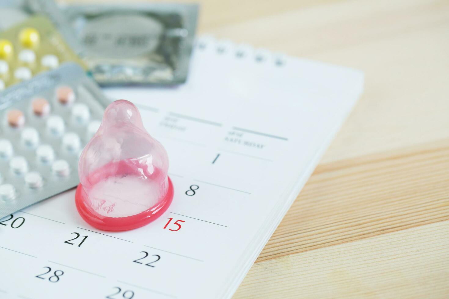 les pilules contraceptives et le préservatif à la date du calendrier calculent la date contrôlent le taux de natalité. fond de table en bois. soins de santé et médecine, concept de contraception. espace vide pour le texte. photo