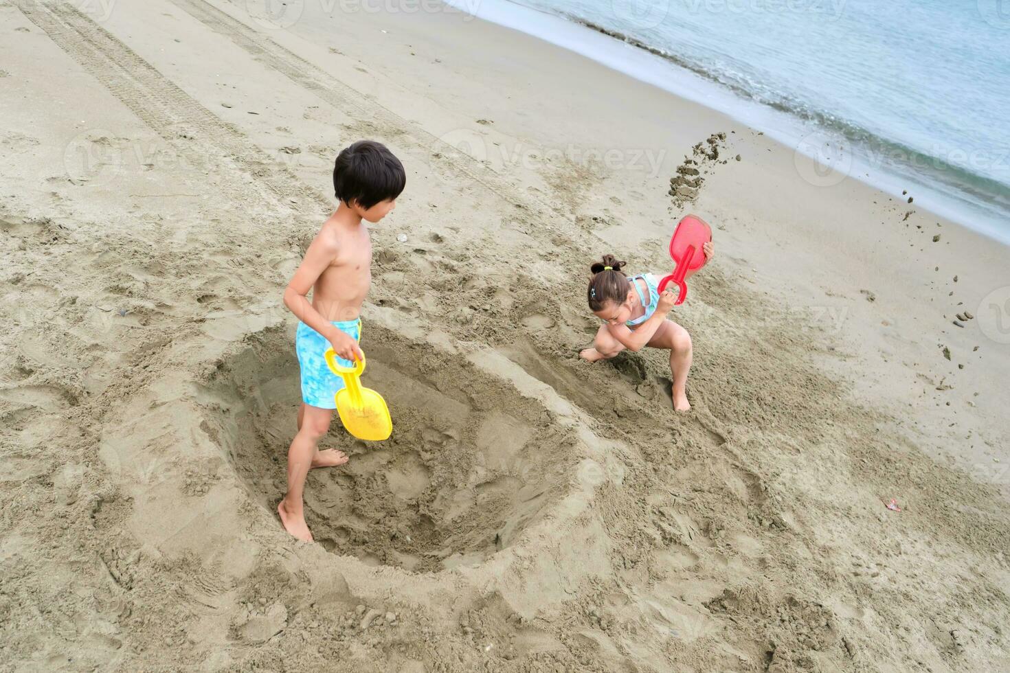 les enfants creuser une trou dans le le sable sur le rivage. photo