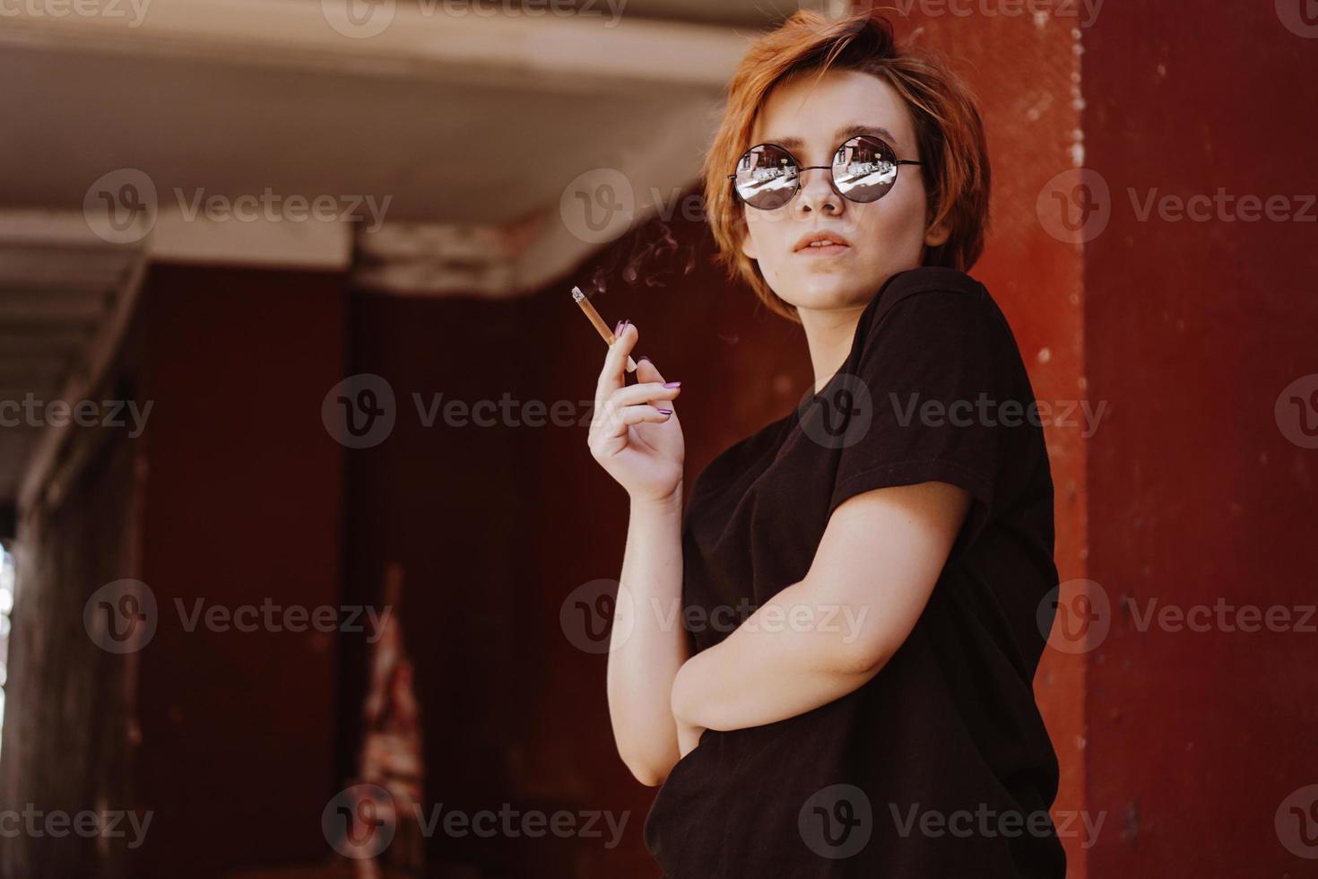 Fille aux cheveux roux courts et lunettes de soleil miroir fumant une cigarette photo