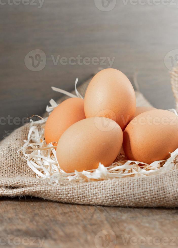 oeufs biologiques frais en toile de jute avec de l'herbe sèche sur une table en bois. photo