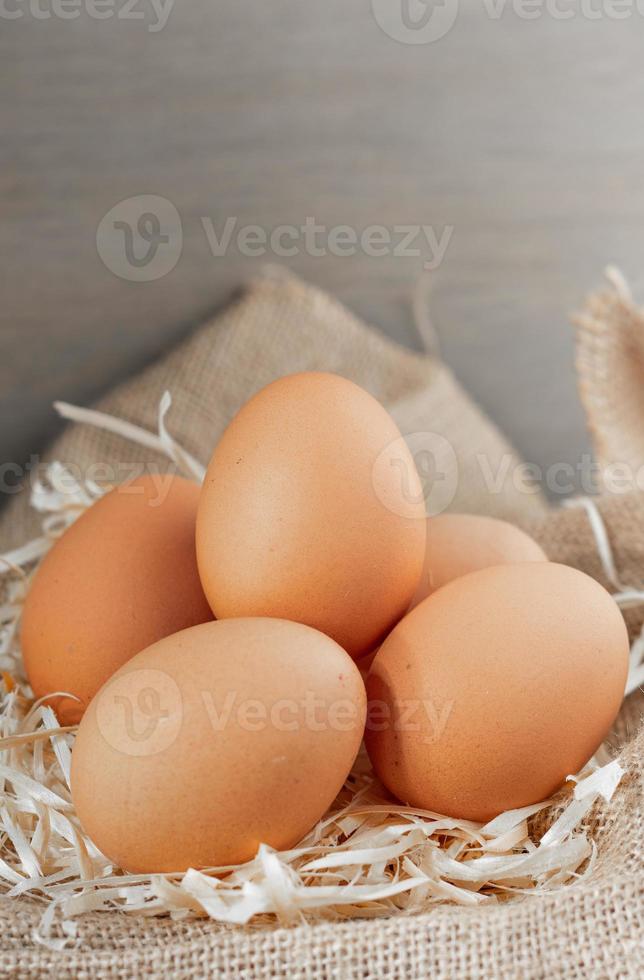 oeufs biologiques frais en toile de jute avec de l'herbe sèche sur une table en bois. photo