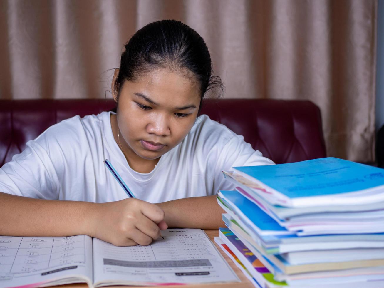 fille faisant ses devoirs sur une table en bois et il y avait une pile de livres. photo