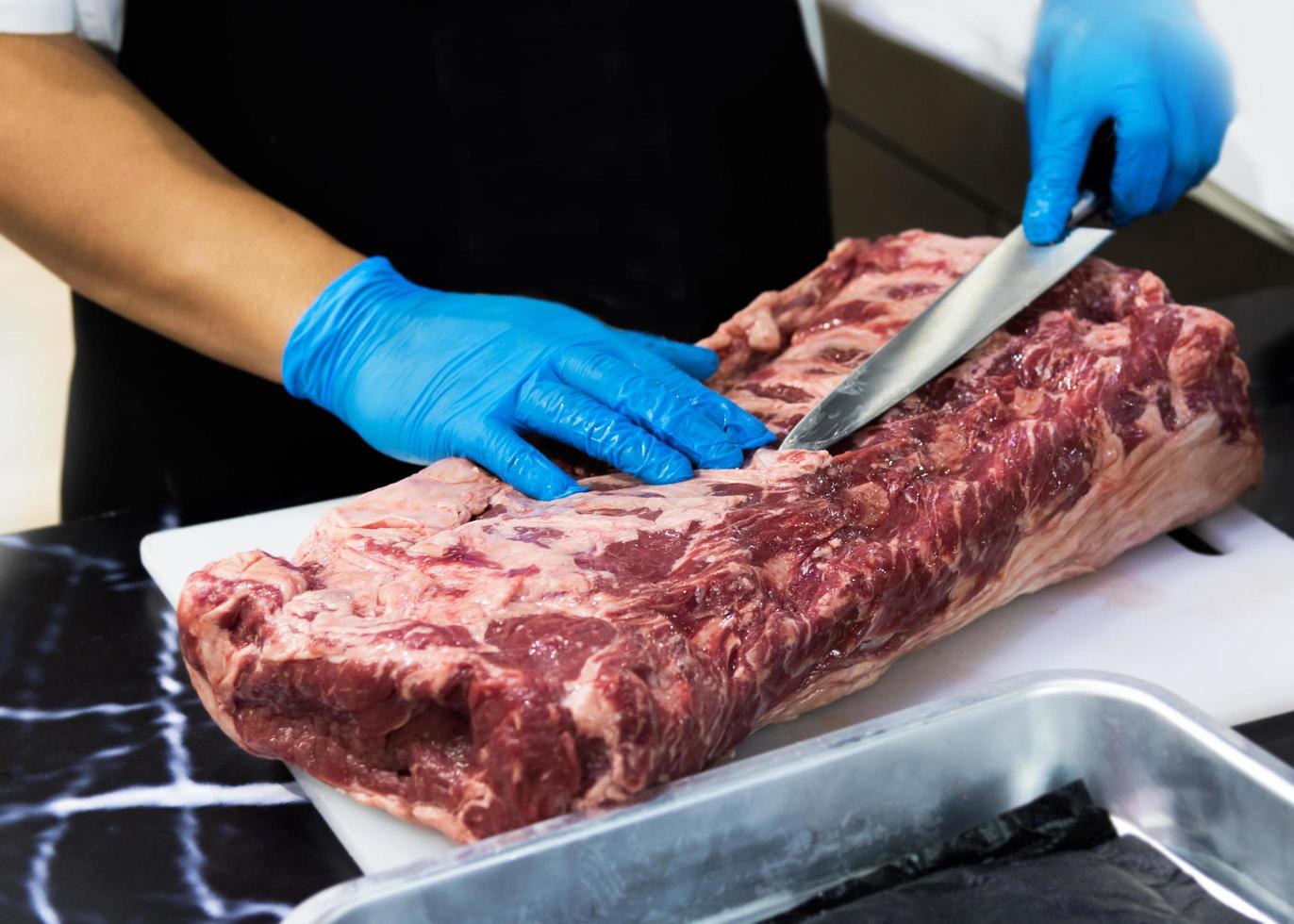 le chef coupe la viande crue avec un couteau sur une planche, le cuisinier coupe la viande crue photo