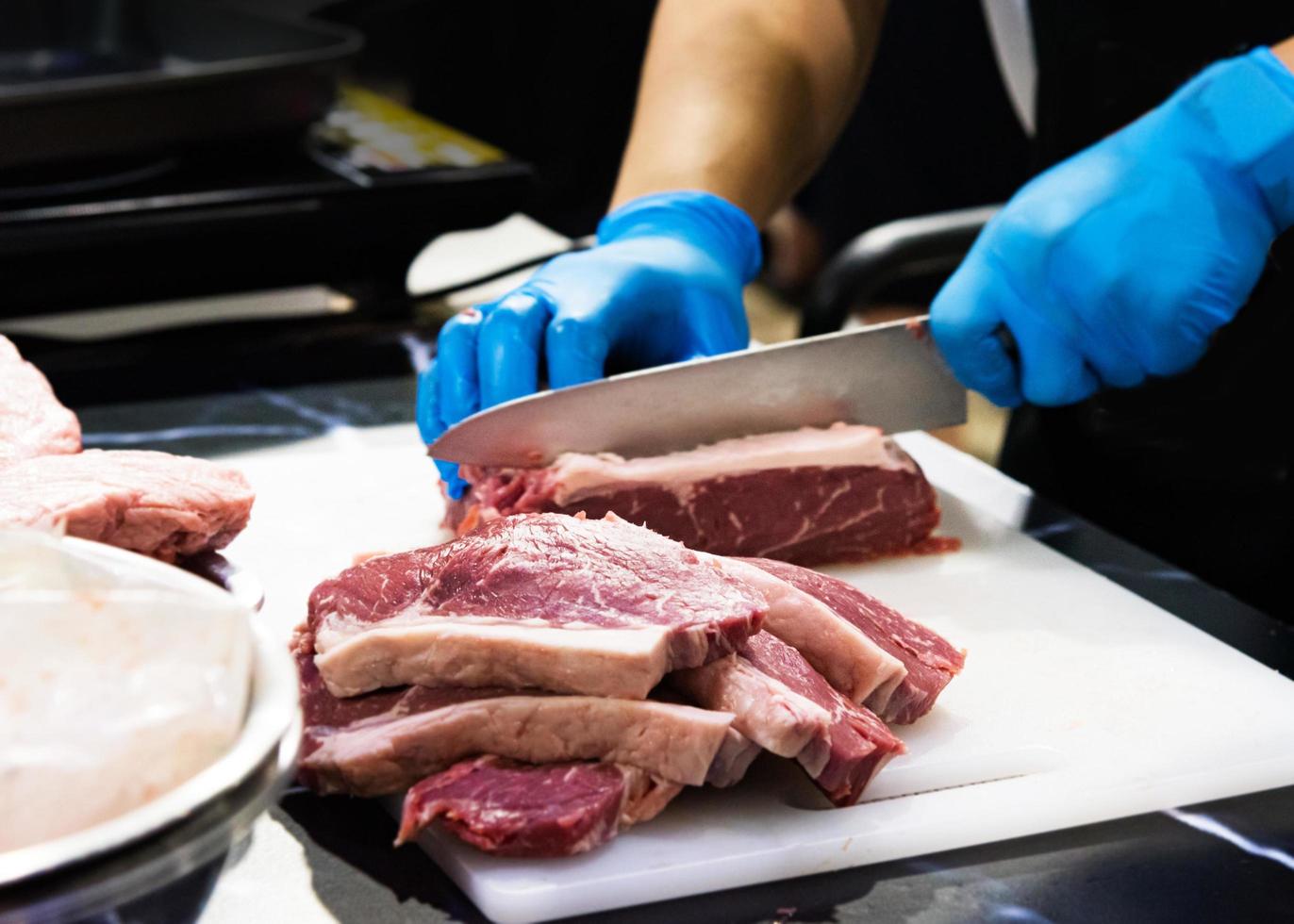 le chef coupe la viande crue avec un couteau sur une planche, le cuisinier coupe la viande crue photo