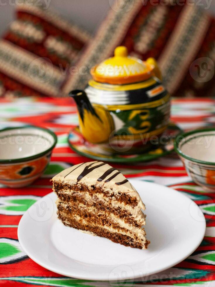 dessert Chocolat gâteau avec beige crème dans Oriental style sur une toit avec une théière et une tasse pour thé. photo