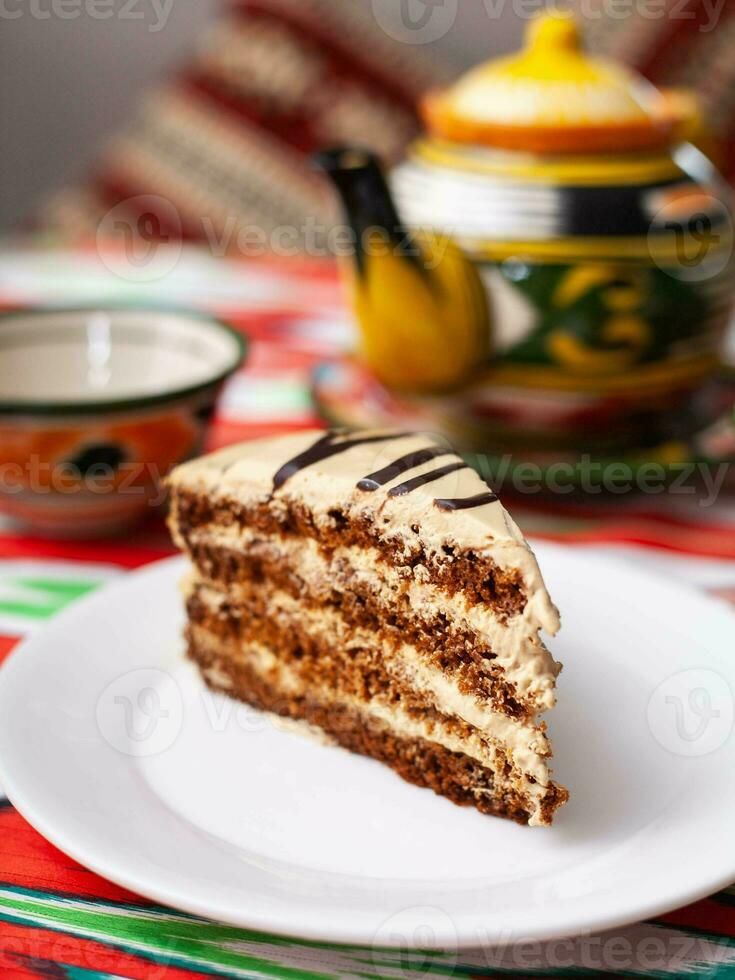 dessert Chocolat gâteau avec beige crème dans Oriental style sur une toit avec une théière et une tasse pour thé. photo