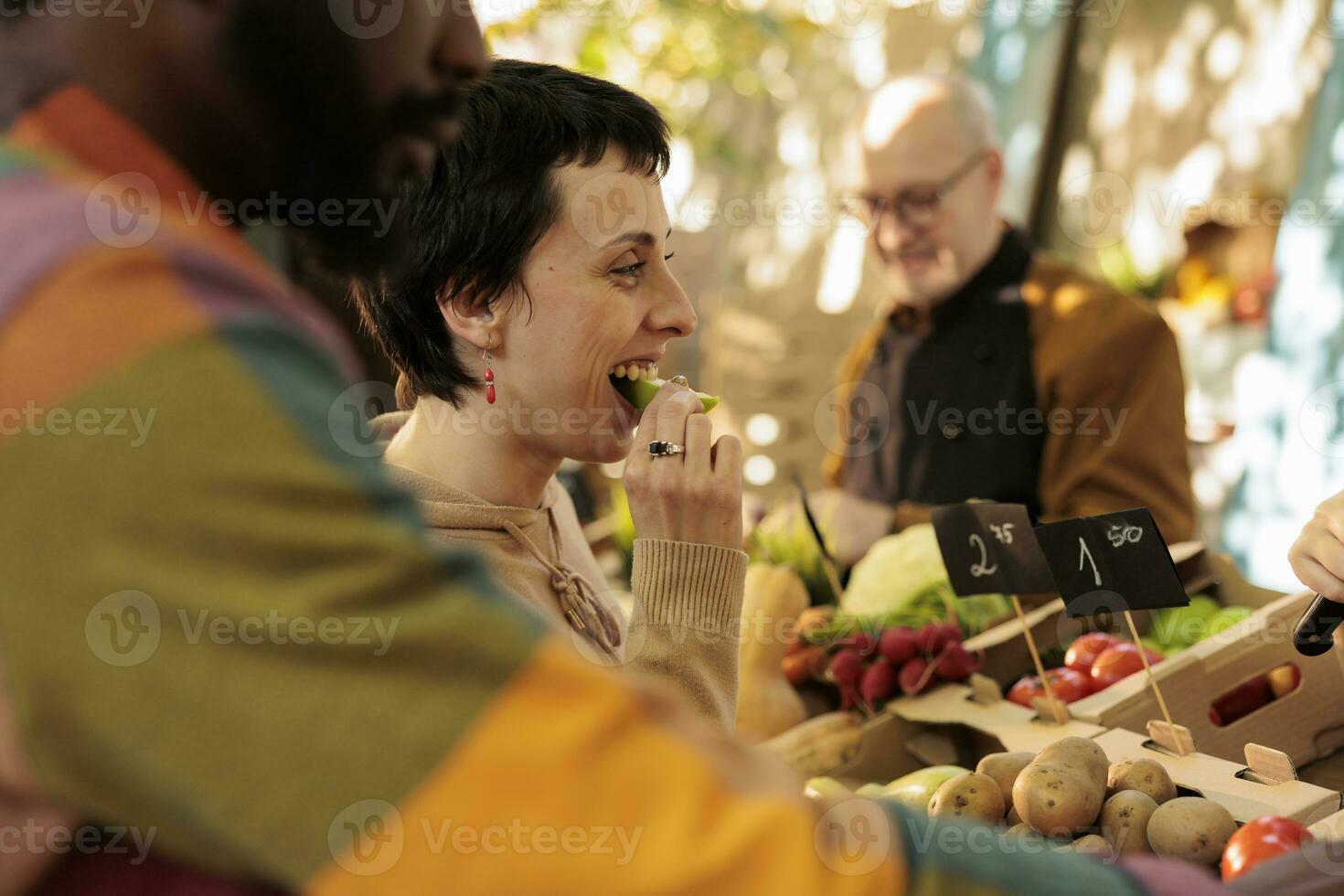 vendeur offre échantillons à les clients tandis que vente fait maison des fruits et des légumes à local Les agriculteurs marché. Jeune multiracial famille couple dégustation Naturel biologique produire tandis que visite nourriture juste photo