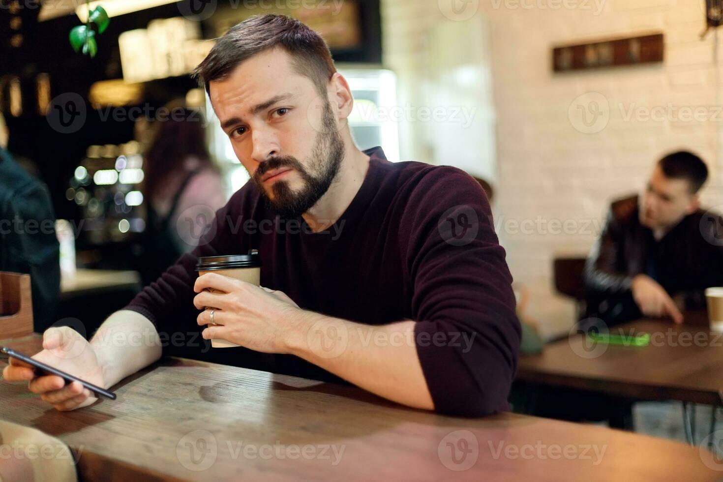 Jeune branché gars envoyer des SMS avec le sien mobile téléphone à le bar photo